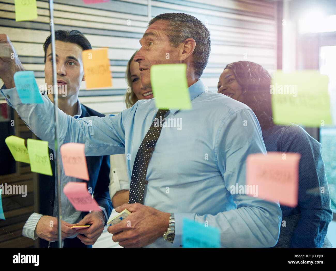 Half body portrait of businessman sticking note on glass, colleagues in background Stock Photo