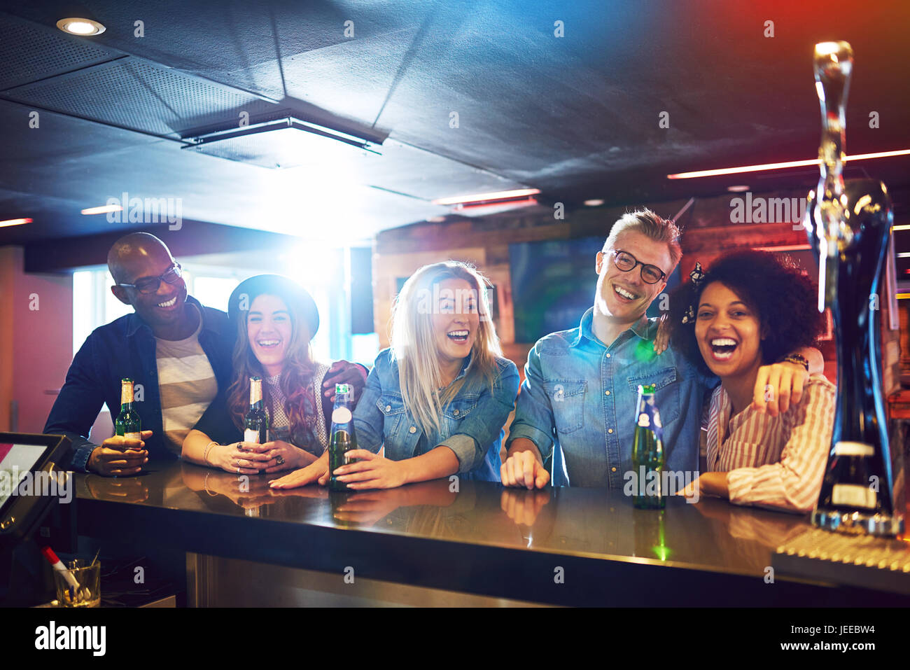 A group of friends inside the bar laughing while communicating and looking at camera. Stock Photo