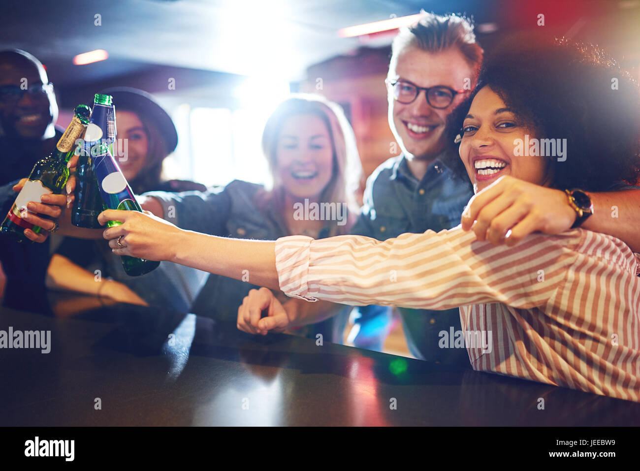 Horizontal indoors shot of happy people smiling and embracing while clanging bottles in the bar. Stock Photo