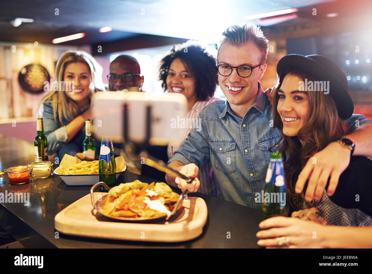 Horizontal indoors shot of people posing for the selfie with snacks and beer at the bar counter. Stock Photo