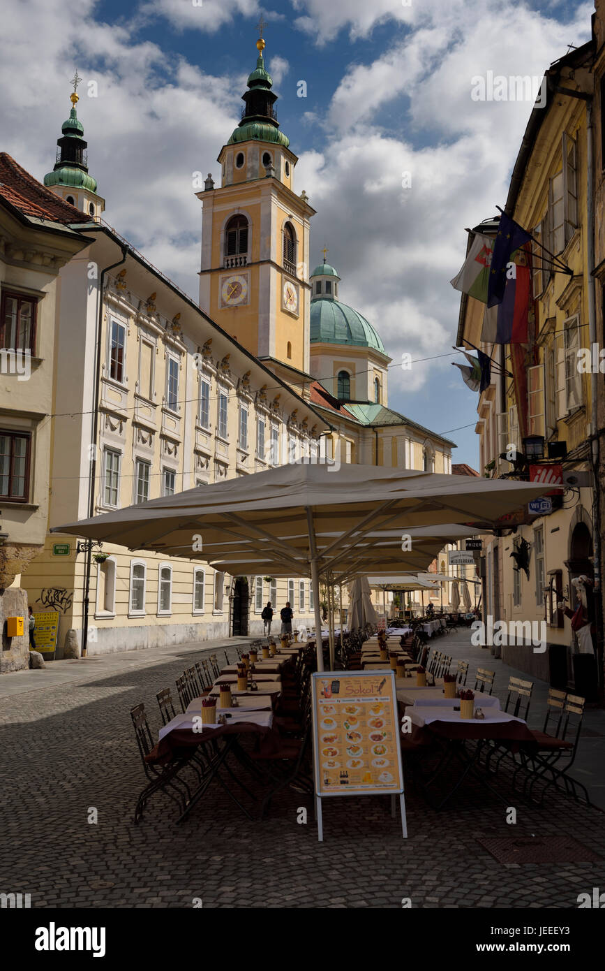 Empty restaurant tables for tourists on the street at Cyril Methodius Square with St. Nicholas church Ljubljana Cathedral in Ljubljana Slovenia Stock Photo