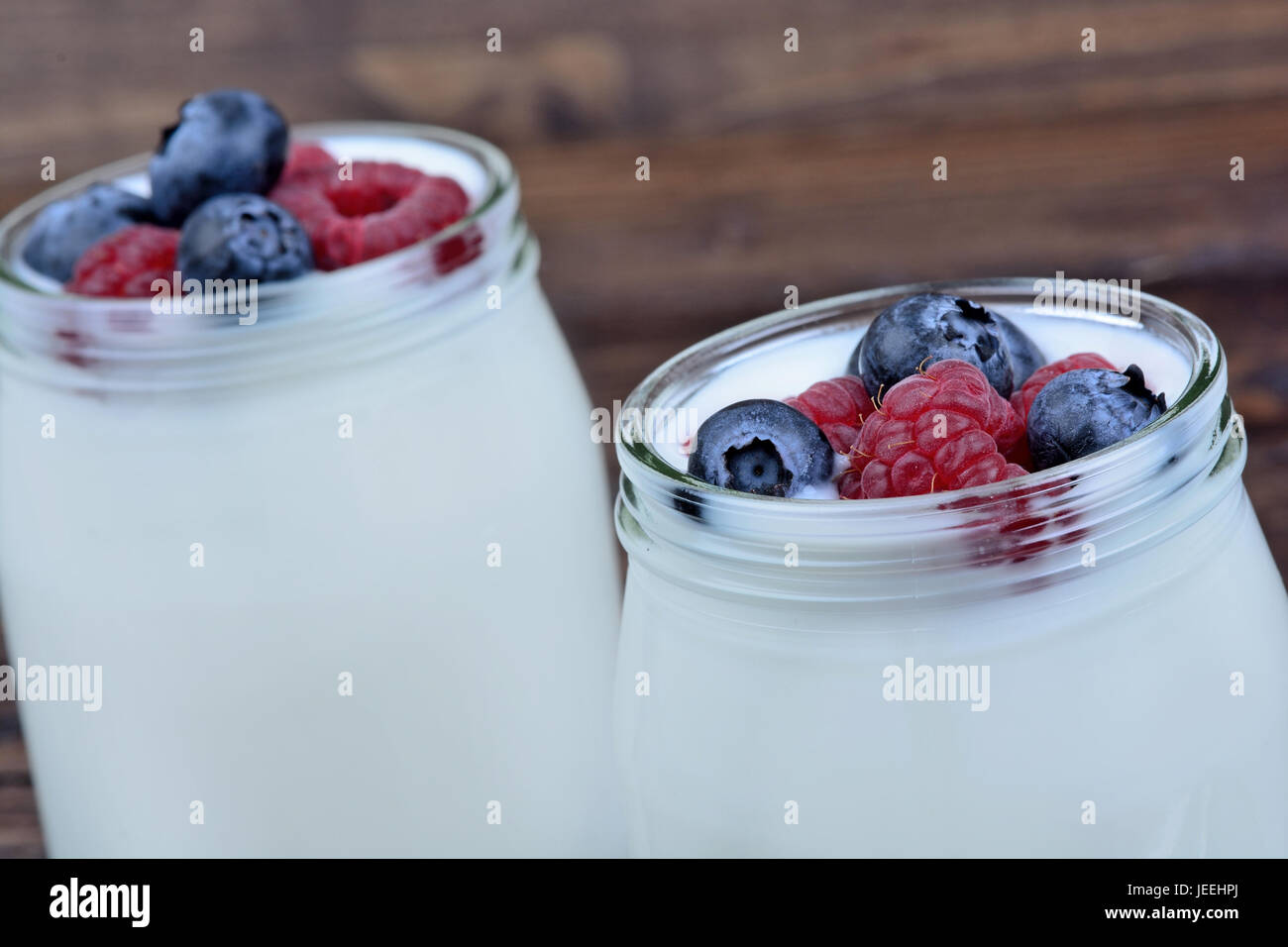 Assorted berries with yogurt in a jars glass on wooden background Stock Photo