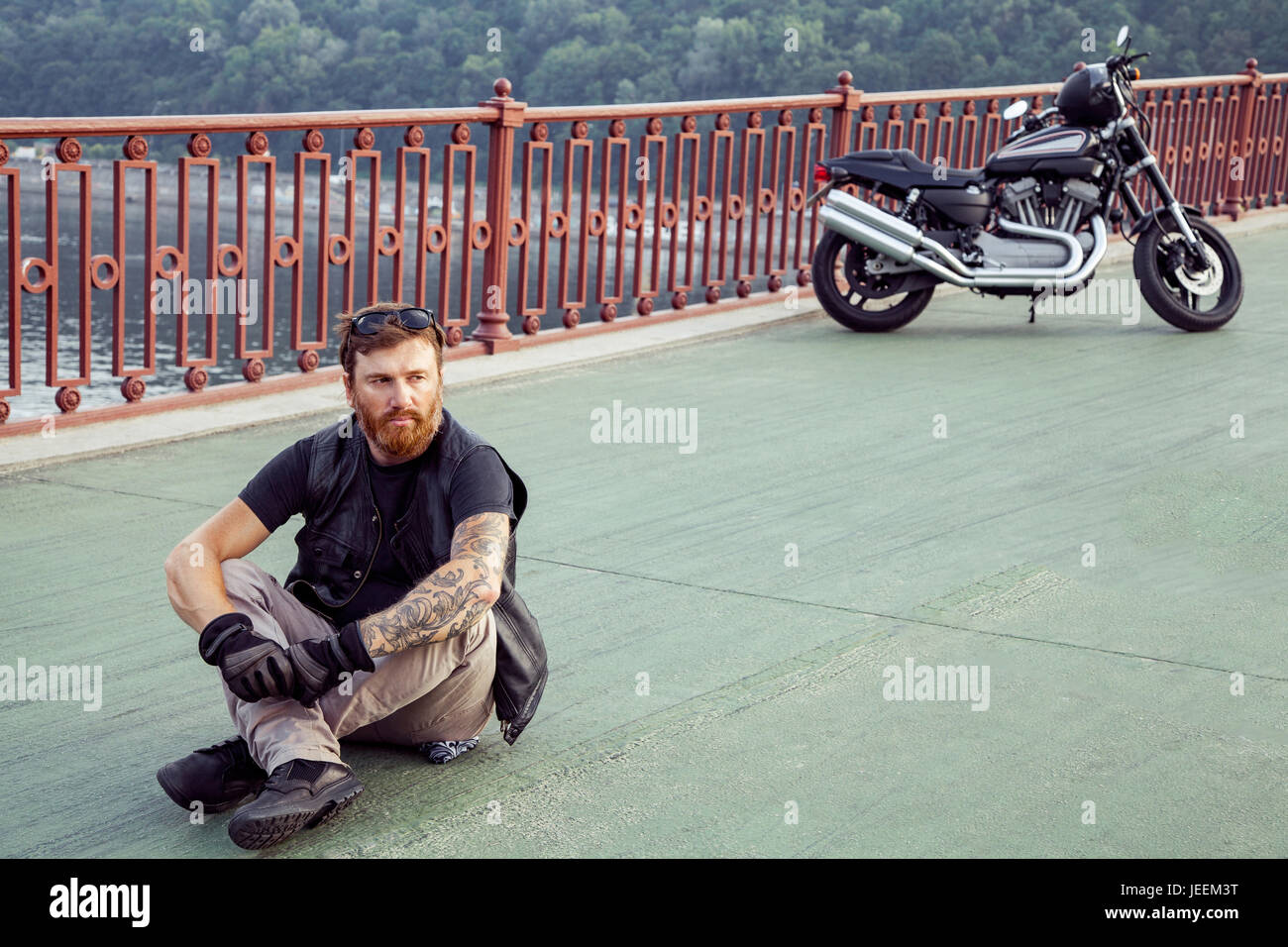 bearded redhead biker with beard in leather jacket sitting on floor. Stock Photo