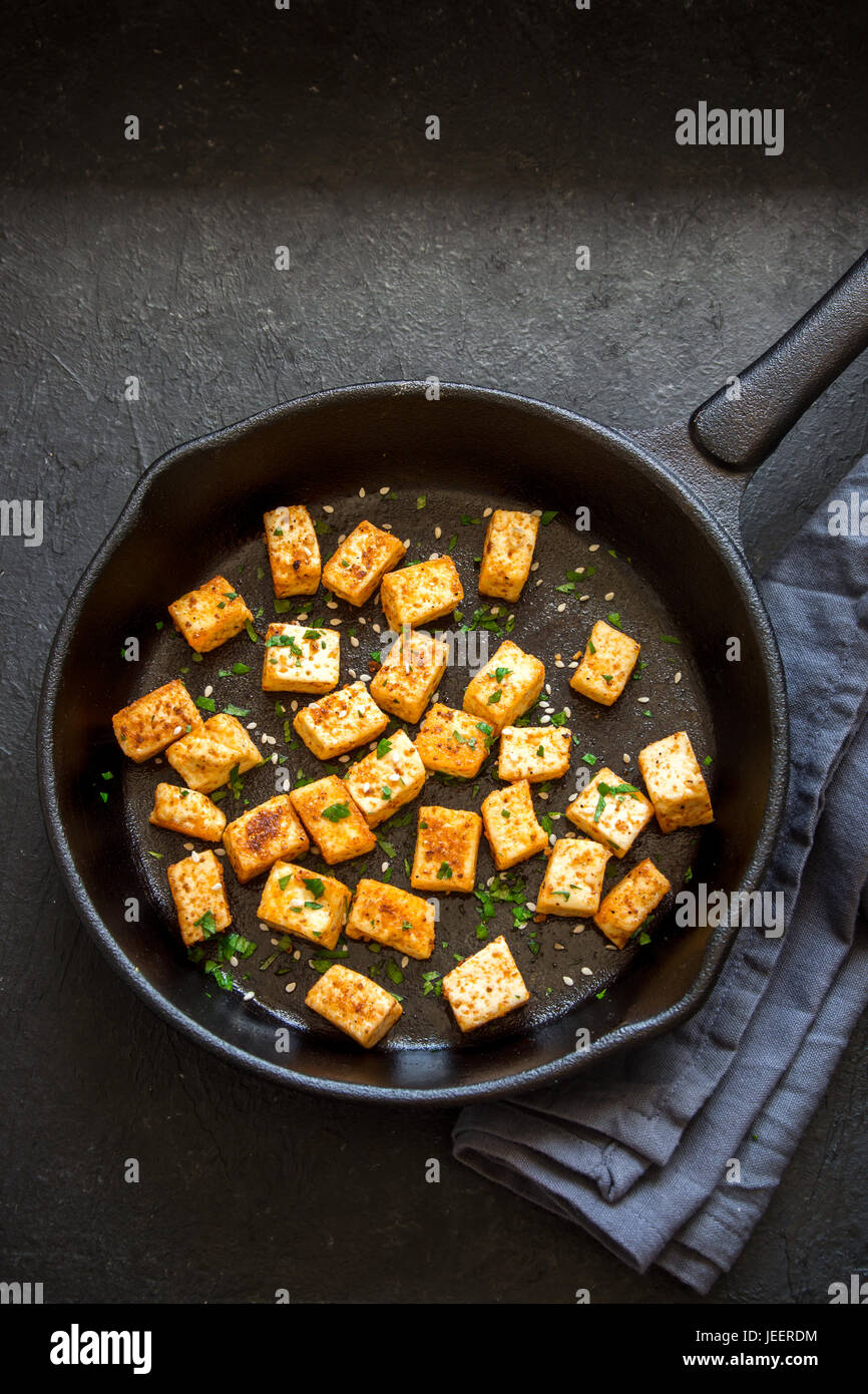 Fried tofu with sesame seeds and spices on cast iron pan, copy space