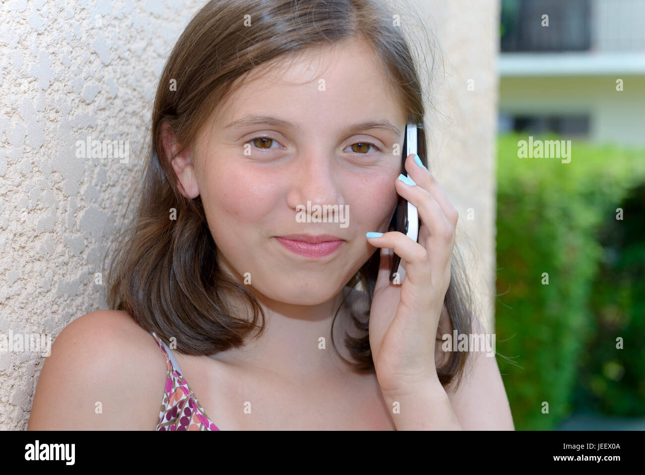 a smiling pre teenager girl calling on smartphone, outdoor Stock Photo