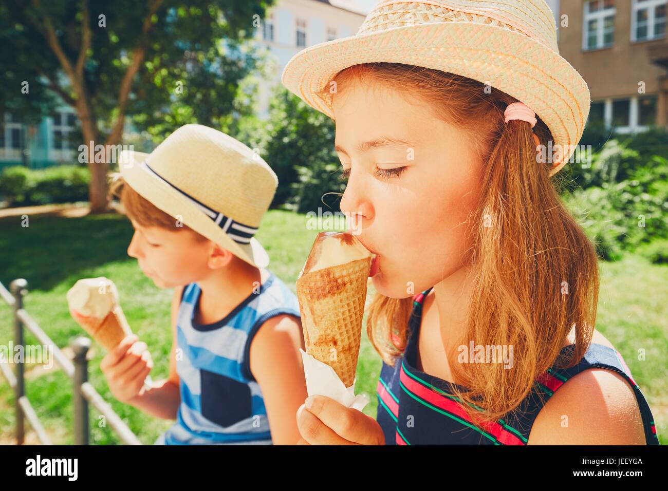 Summer day in the city. Cute siblings with hats eating big ice cream in the park. Stock Photo