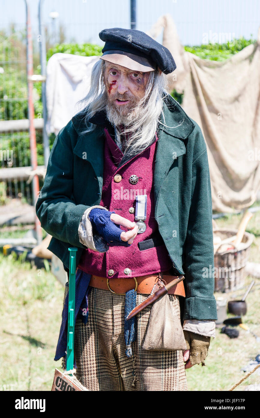 Down and out Navy, senior old man, Victorian character re-enactment. Filthy dirty wears green jacket, red waistcoat and medal. Facing, eye-contact. Stock Photo