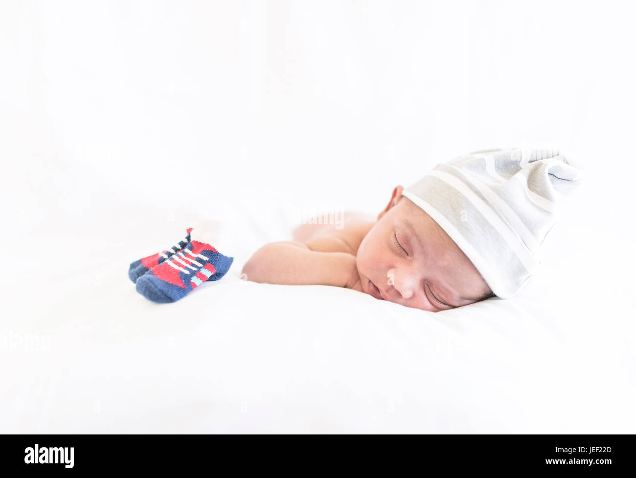 Model released photograph of a newborn baby with a cap sleeping on his tummy Stock Photo