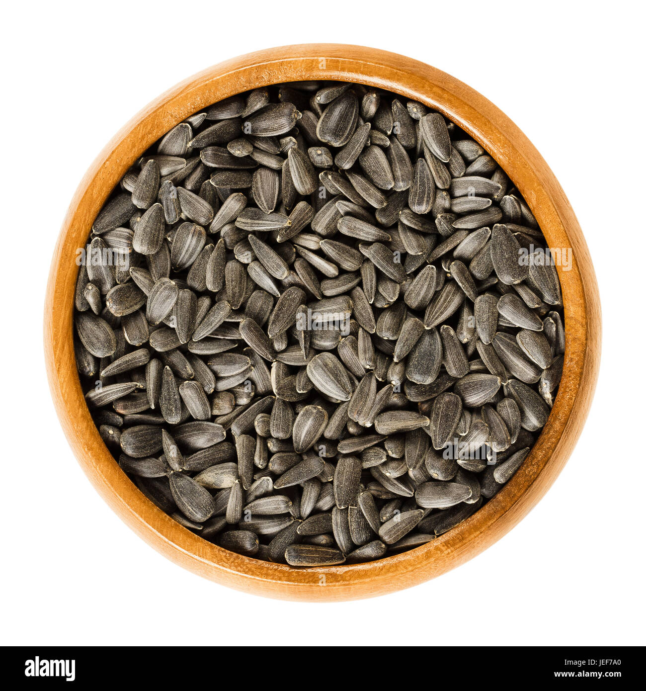 Sunflower seeds in wooden bowl. Fruits of the oilseed Helianthus Annuus, the common sunflower. Whole seeds with black hulls. Isolated macro food photo Stock Photo