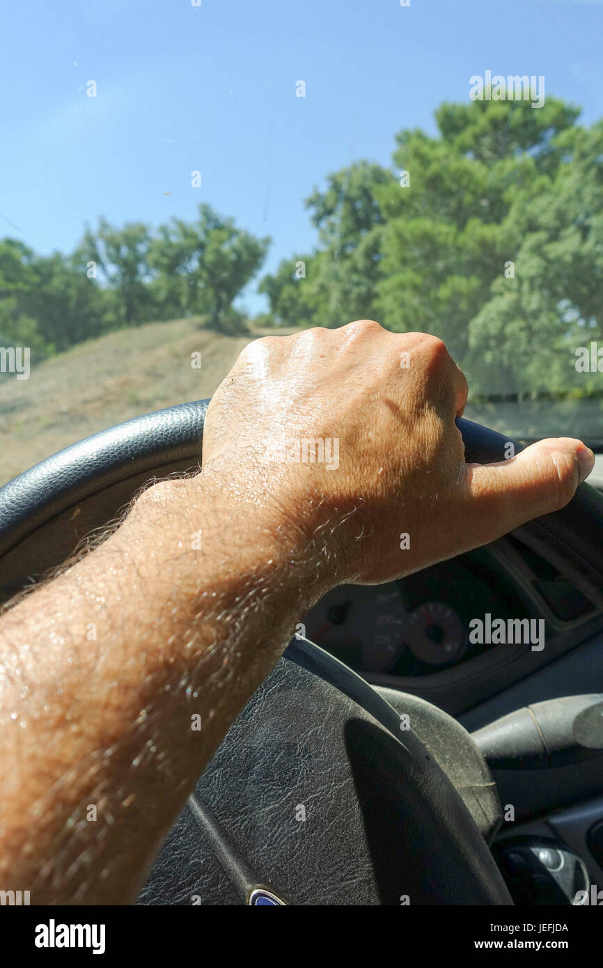 Wet sweat hand, on steering wheel, inside car, close up, dry mediterranean forest. Spain. Stock Photo