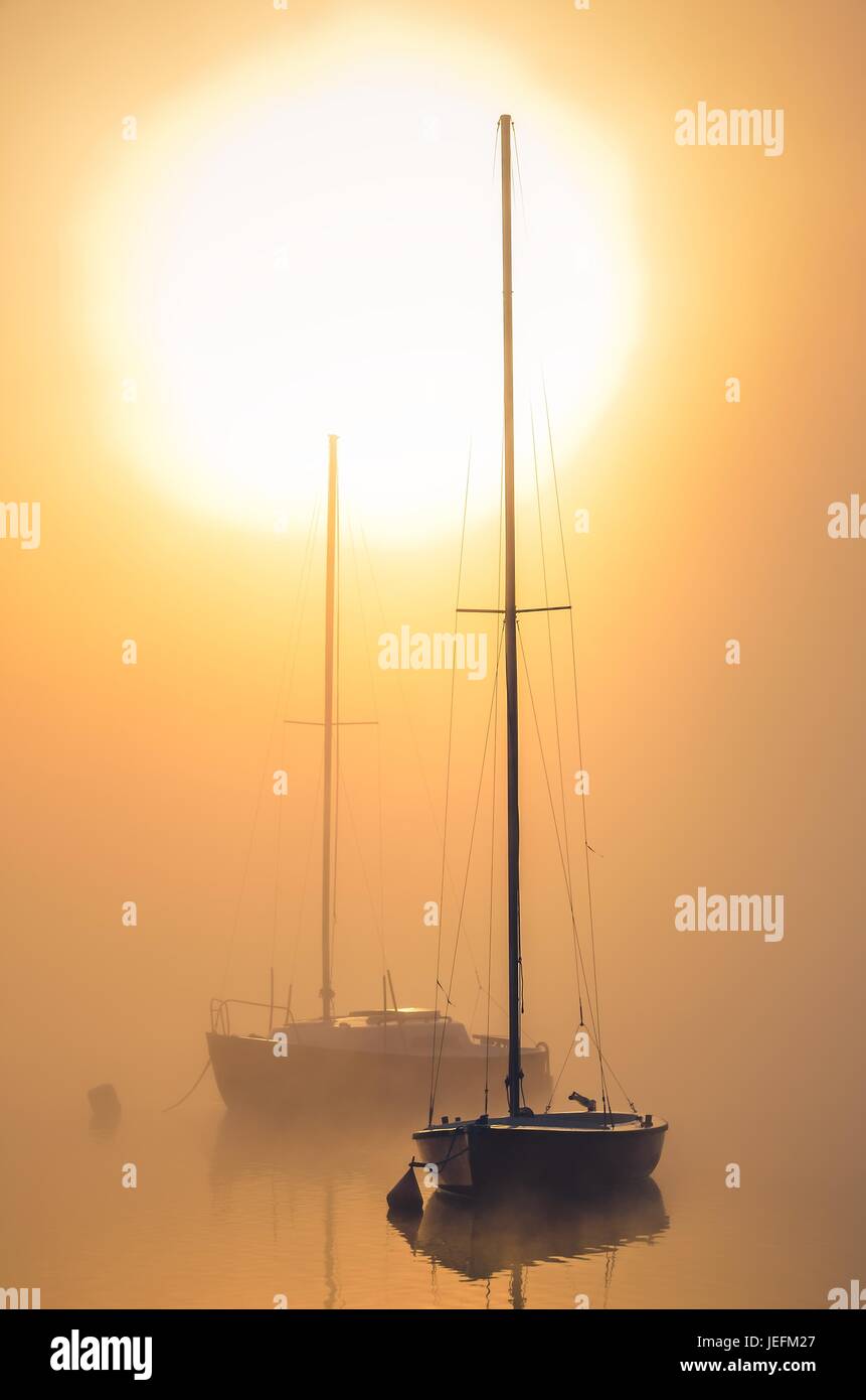 Morning foggy landscape. Boats on the lake with the rising sun in the background. Stock Photo