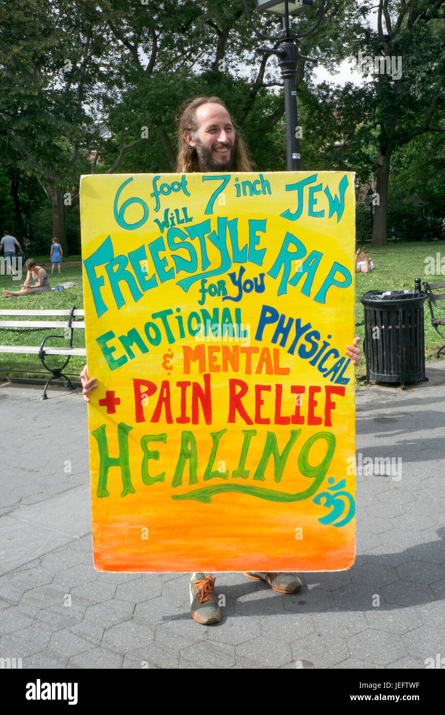 A tall busker with a colorful sign soliciting donations in Washington Square Park in Greenwich Village, Manhattan, New York City. Stock Photo