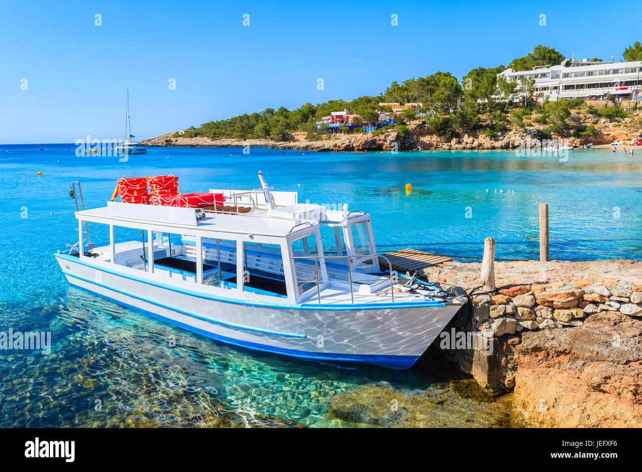 White and blue colour ferry boat for tourists mooring in Cala Portinatx