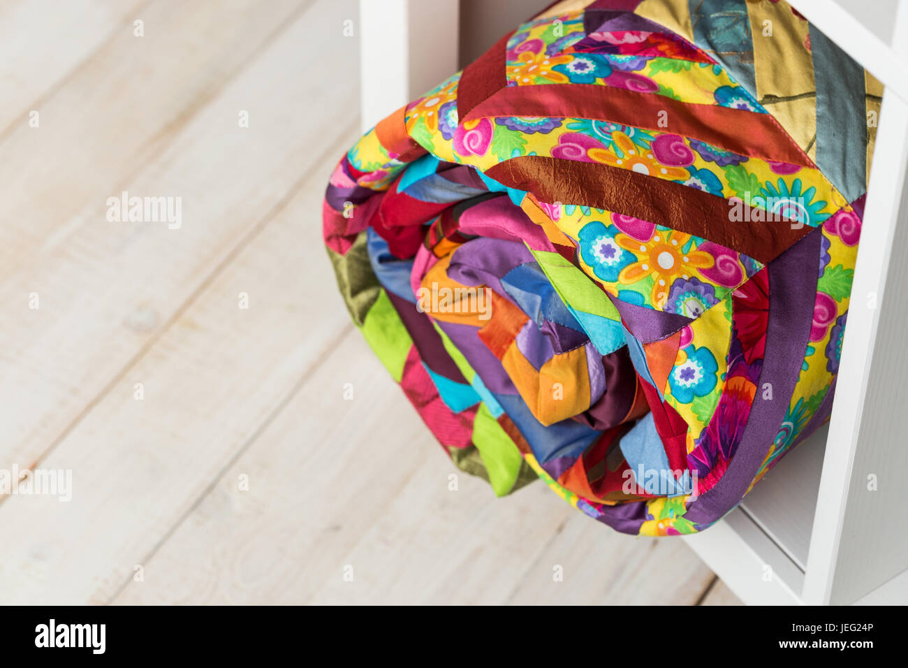 patchwork, sewing and fashion concept - beautiful colorful quilted blanket at white shelves in studio, background of white floor in a warehouse, finished stitched coverlet, top view. Stock Photo