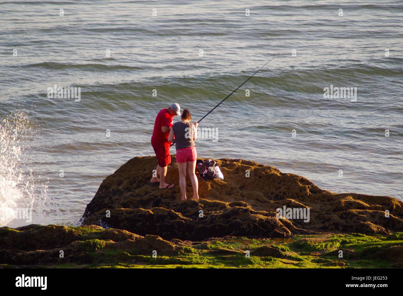 A Couple Sea-Fishing From a Rock on the Beach with oncoming Waves Exmouth, Devon, UK. June, 2017. Stock Photo