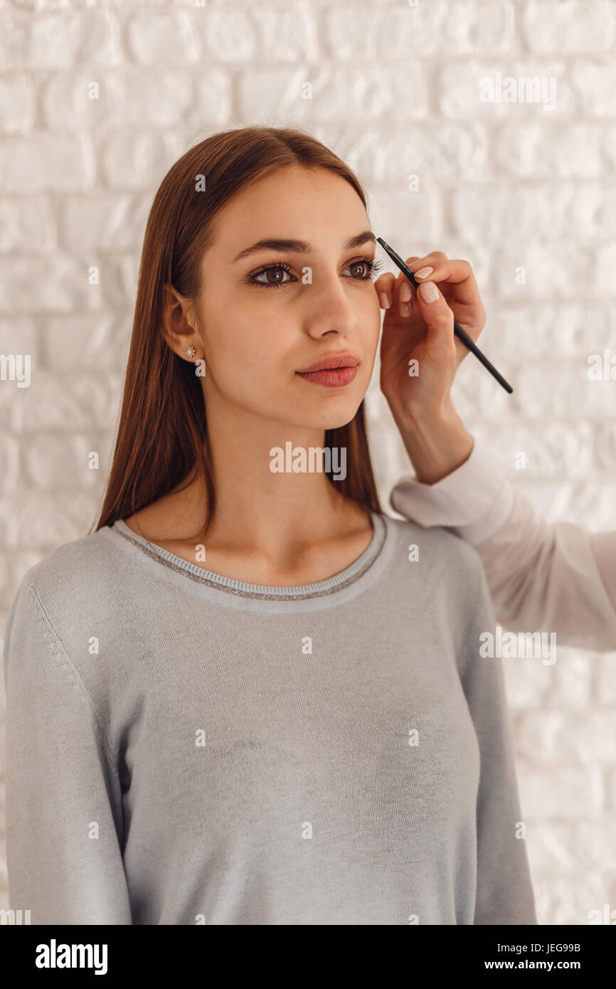 Beautiful woman and cosmetologist drawing a shape of eyebrows using cosmetic brush Stock Photo