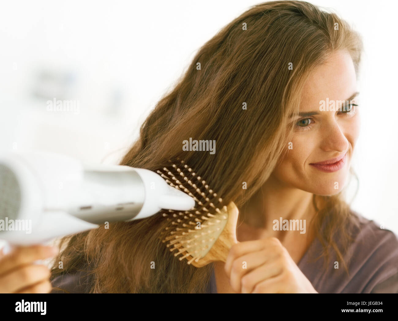 Happy woman brushing and blow drying hair in bathroom Stock Photo