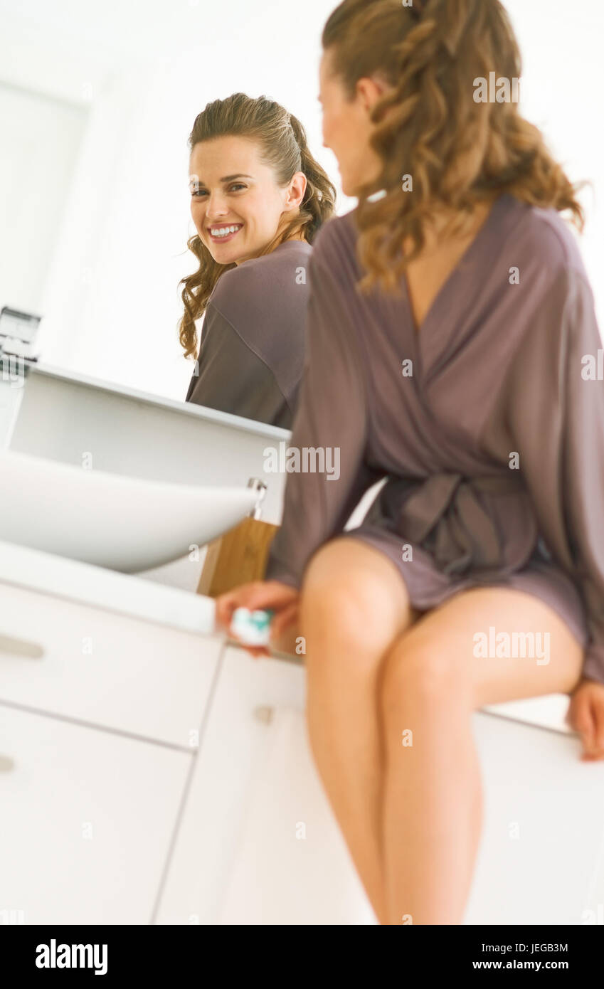 Happy young woman looking in mirror in bathroom Stock Photo - Alamy