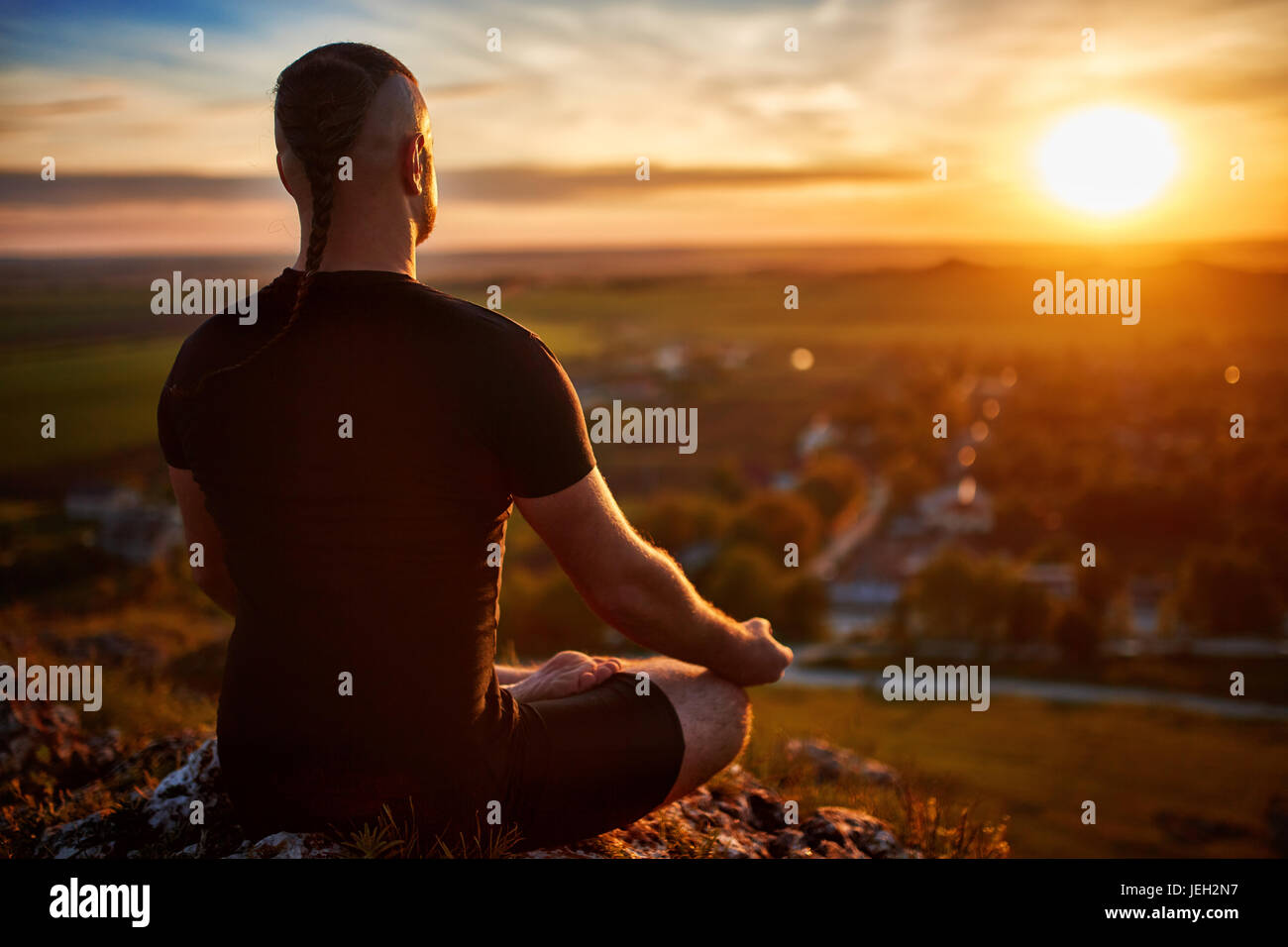 Rear view of the man meditating yoga in lotus pose on the rock at ...