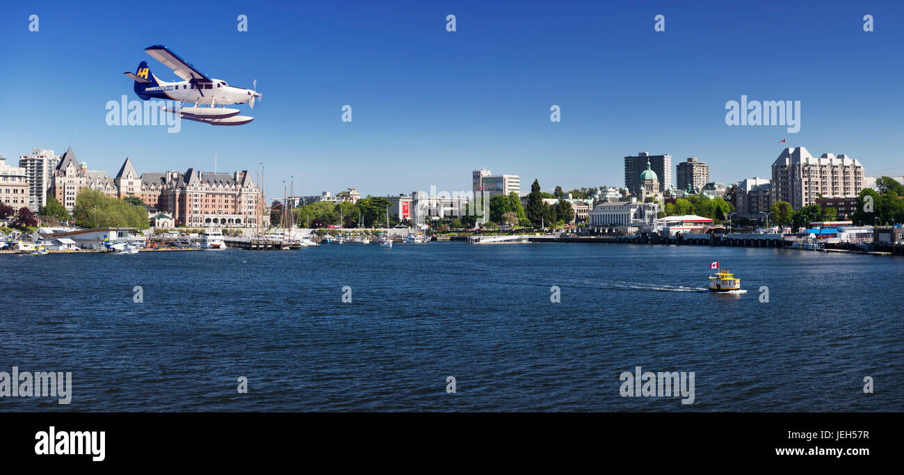 Harbour Air seaplane landing on water and H2O taxi sea taxi boat in front of a panoramic scenery of Victoria BC harbour front skyline. Victoria, Vanco Stock Photo
