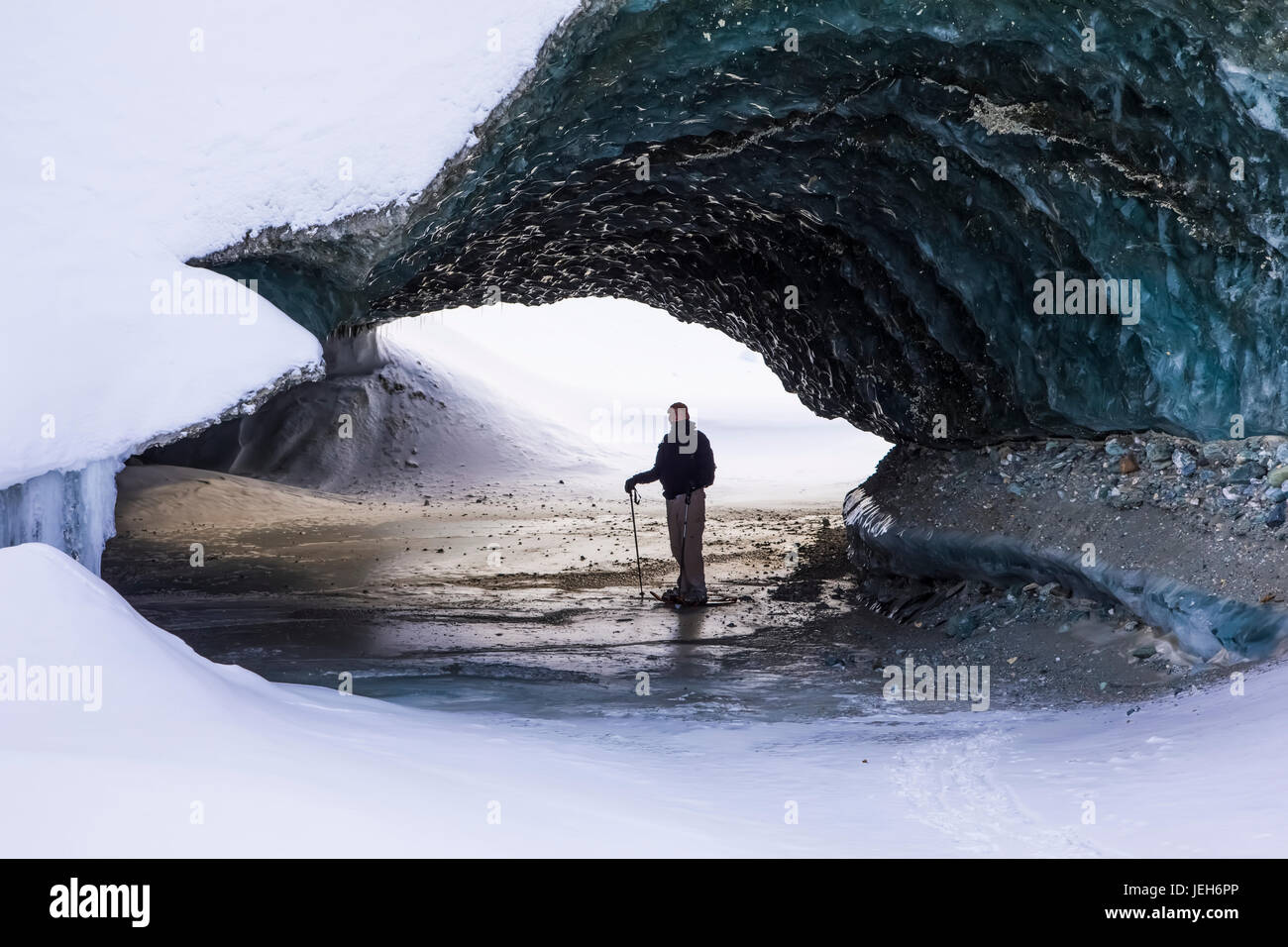 A man on snowshoes stands beneath the ice of Canwell Glacier in the Alaska Range in winter; Alaska, United States of America Stock Photo