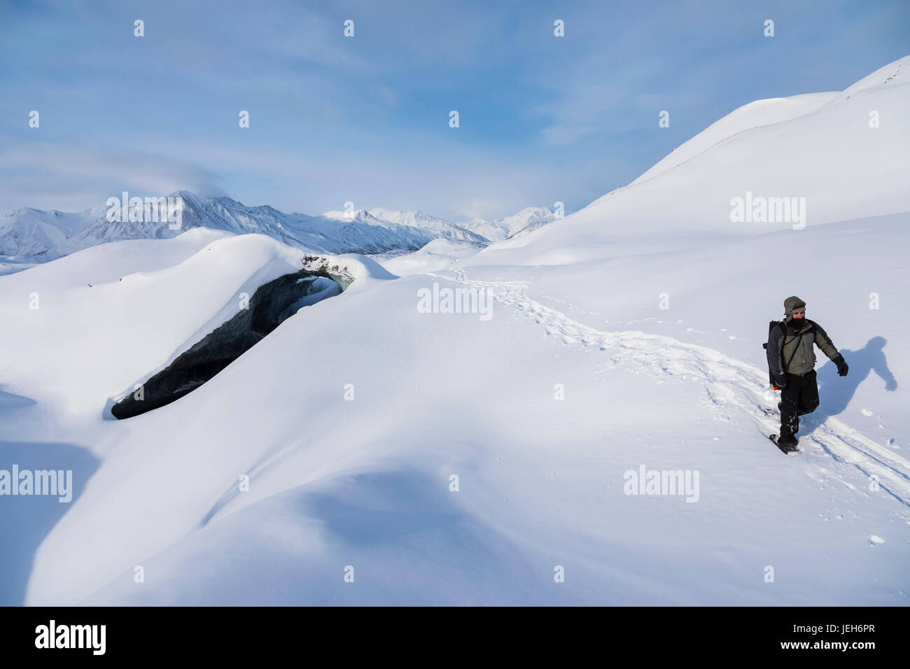 A snowshoer crosses over the snow-covered Canwell Glacier in winter; Alaska, United States of America Stock Photo