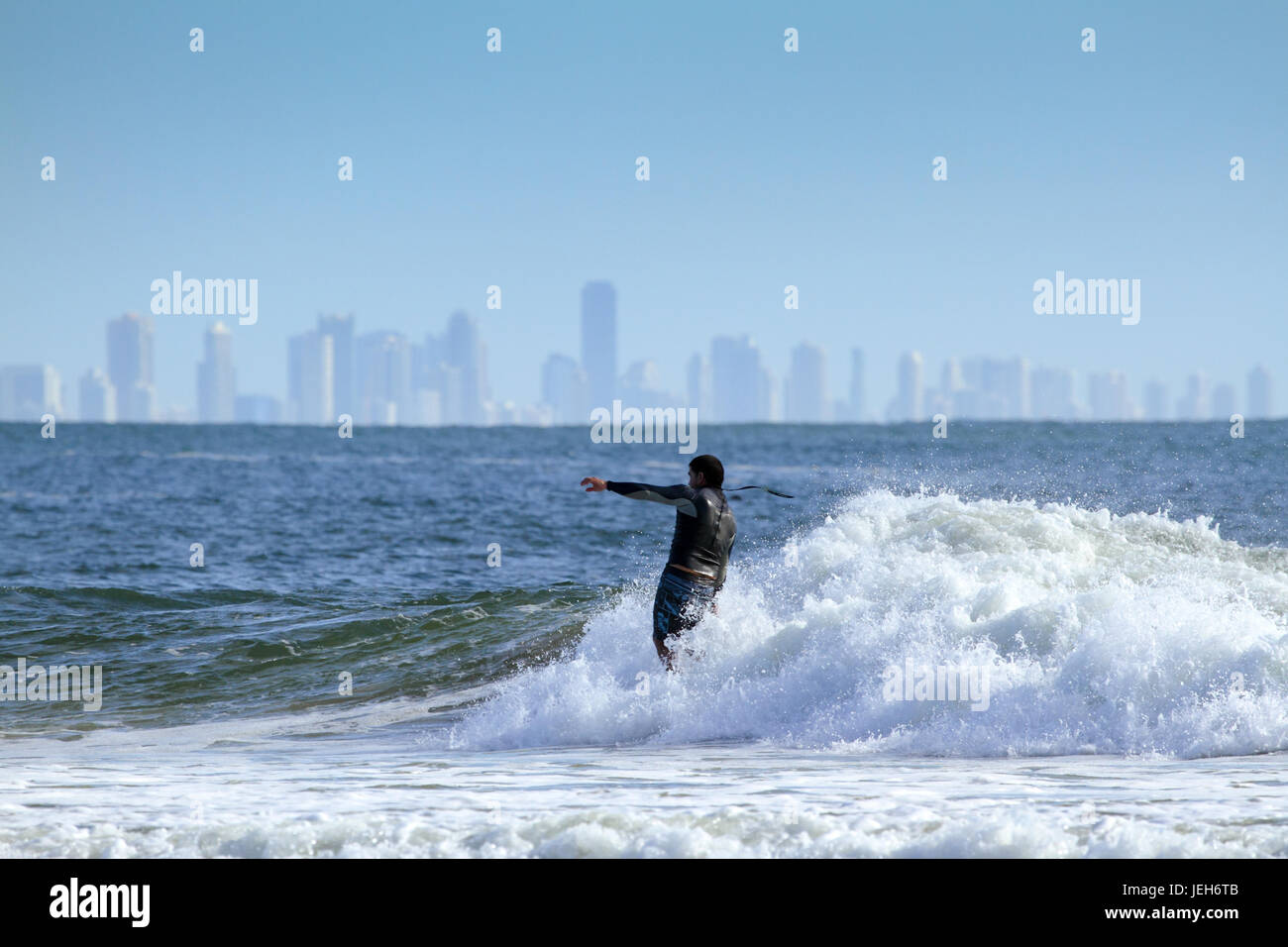 A man surfing with Surfers Paradise in the background. Stock Photo