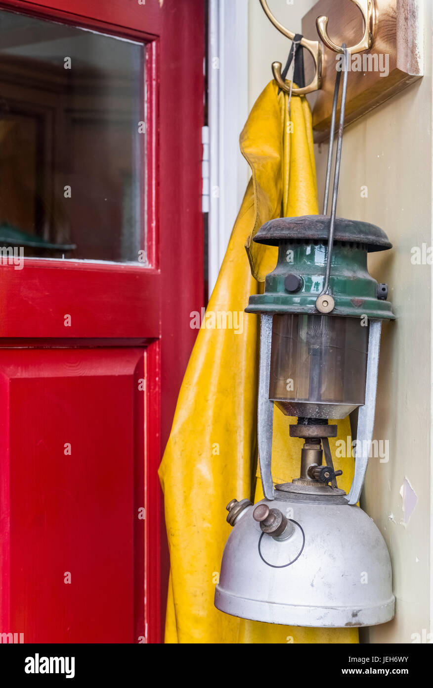 A lantern and yellow rain jacket hang beside a red door; Yorkshire, England Stock Photo