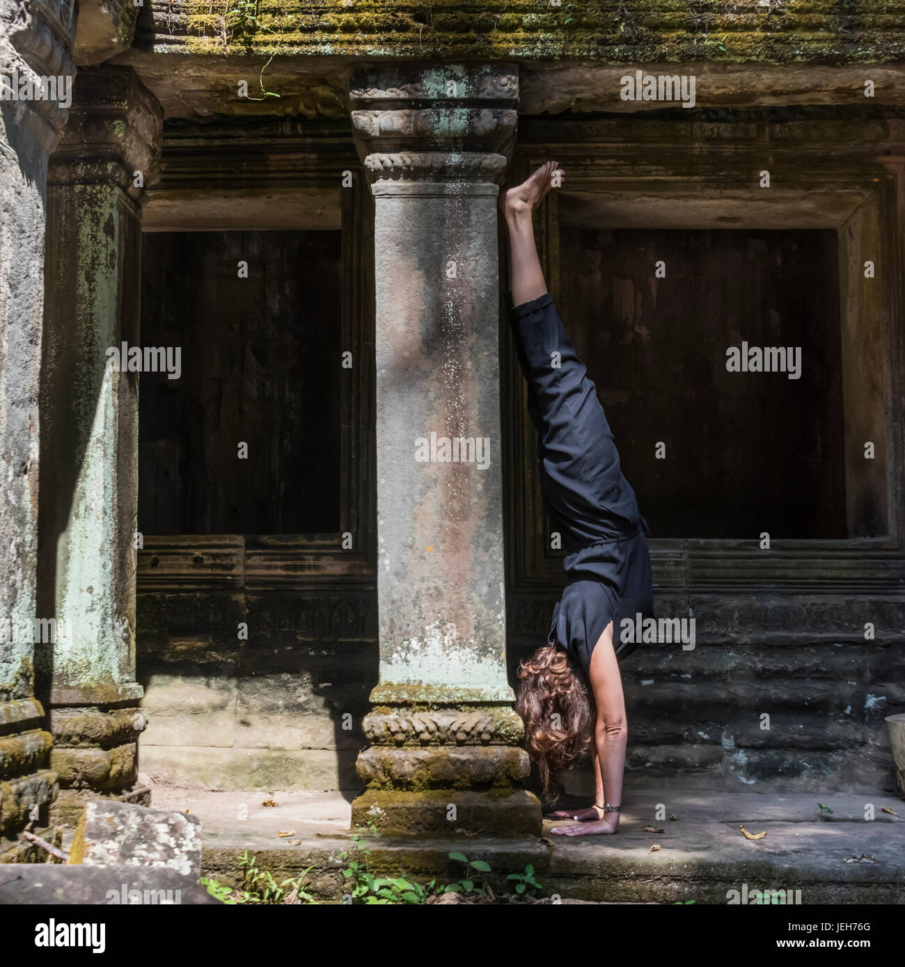 A woman does a hand stand at Ta Prohm Temple; Krong Siem Reap, Siem Reap Province, Cambodia Stock Photo