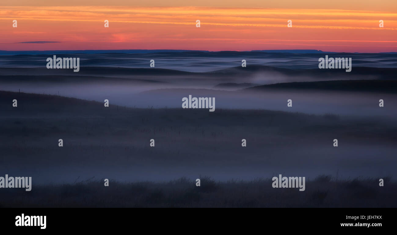 Sunrise colour and fog coat the Grasslands National Park in an eerie mist; Saskatchewan, Canada Stock Photo