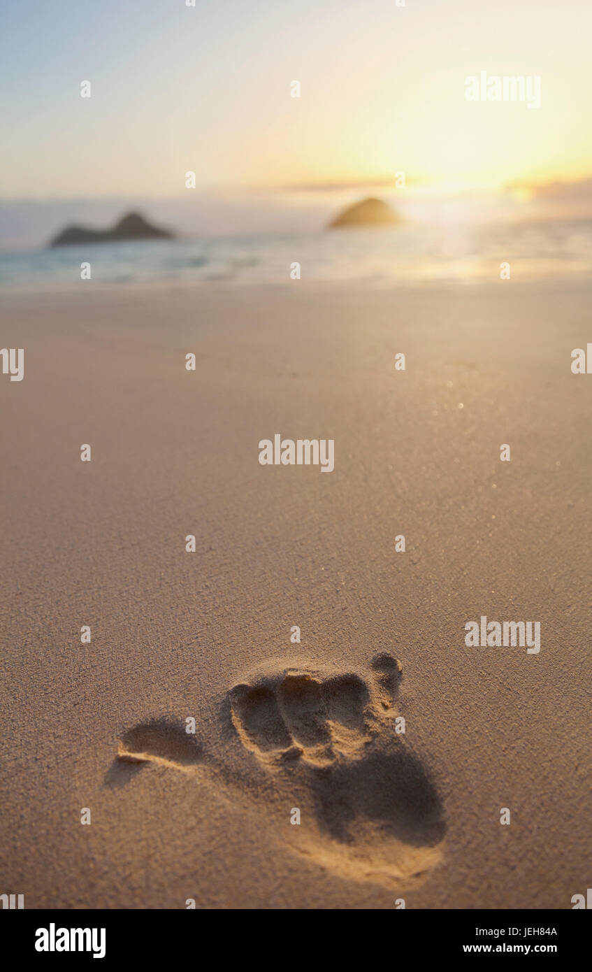 Shaka hand print in the sand with a view of Mokulua twin islands and the ocean at sunset in the distance Stock Photo