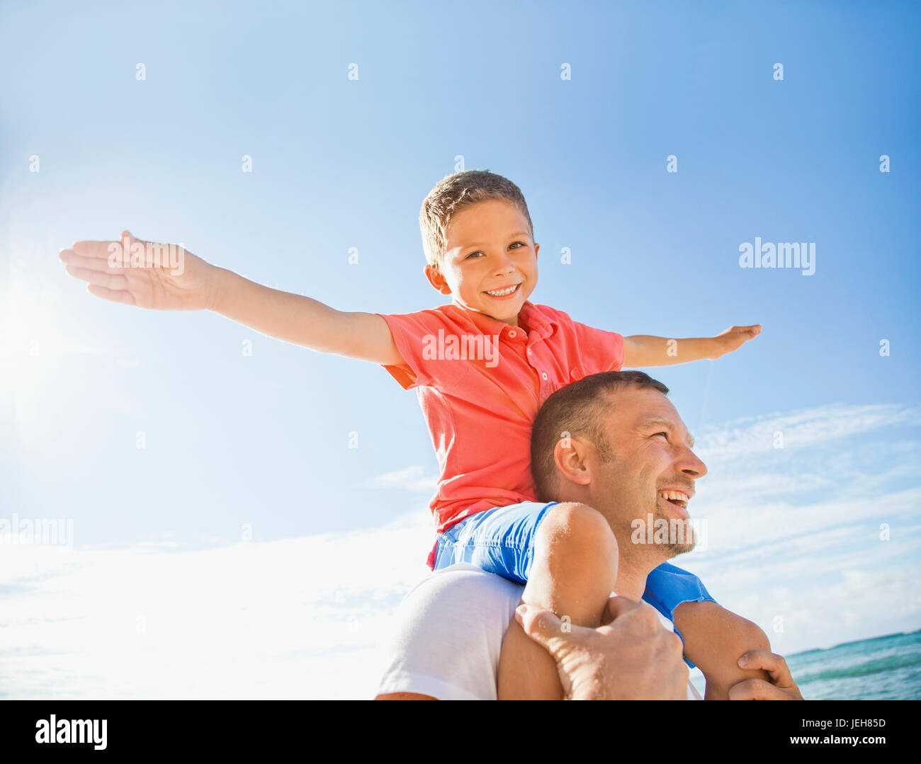 A boy piggybacking on his dad flying like an airplane with his arms; Honolulu, Oahu, Hawaii, United States of America Stock Photo