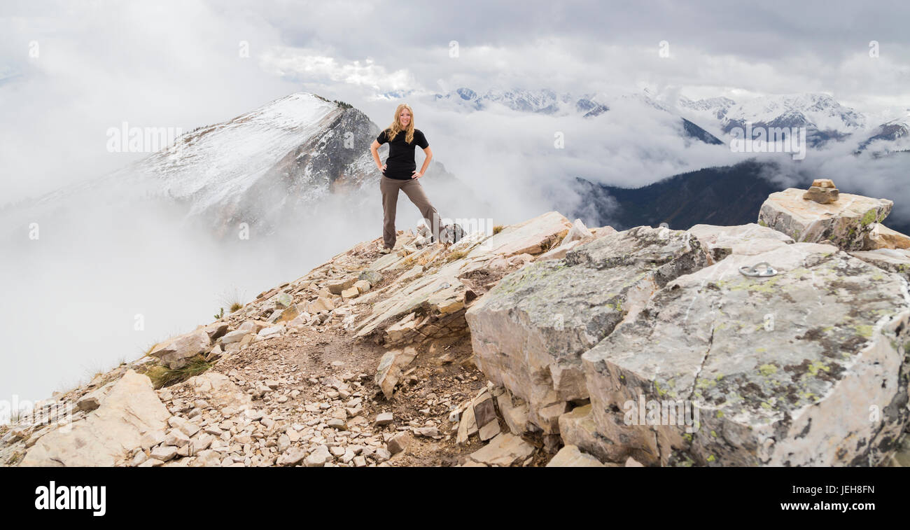 A female hiker poses alone for an adventurous portrait at the peak of a mountain on the hiking trails of Kicking Horse Mountain in the Rocky Mountains Stock Photo
