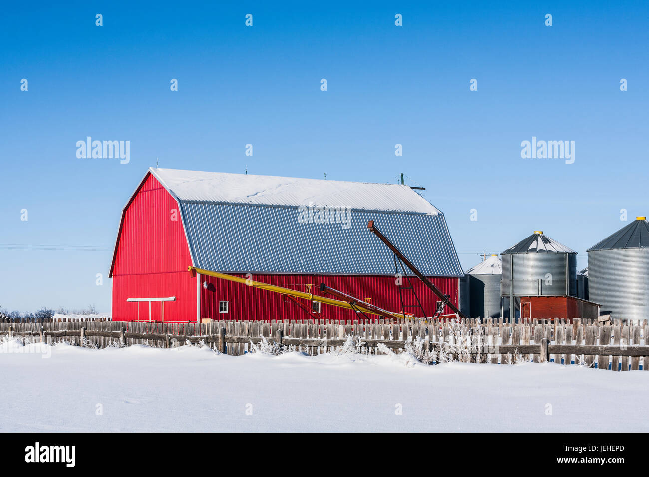 A bright red barn with a snowy field and wooden fence in the foreground ...