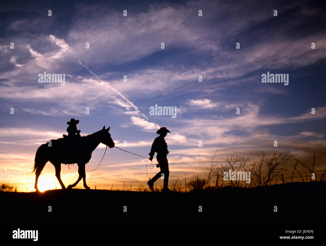 Agriculture - A cowboy leads his young daughter on a horse at sundown while carrying a fishing pole / Childress, Texas, USA. Stock Photo