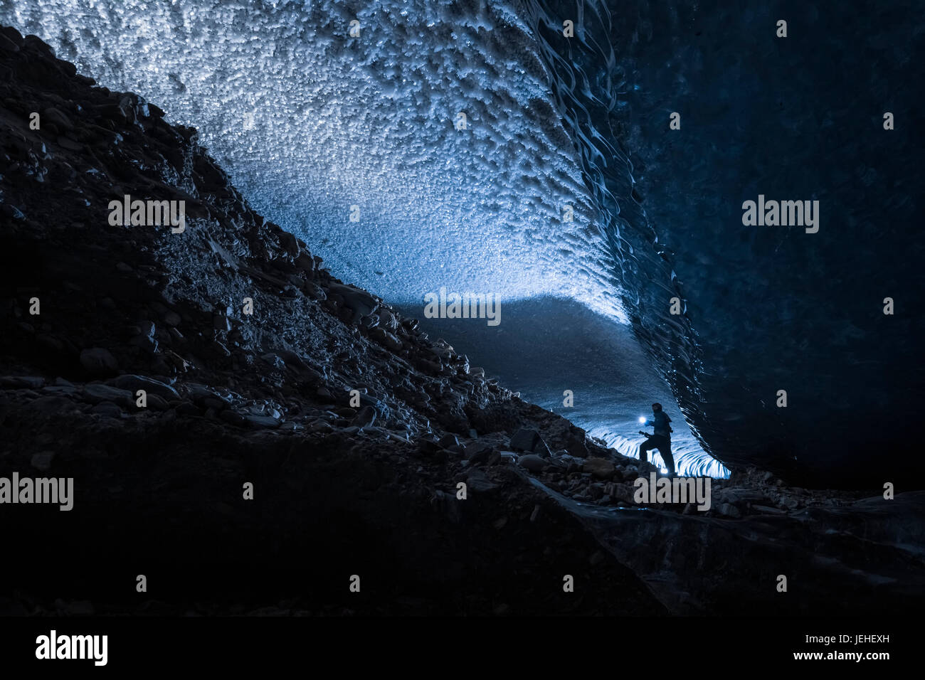 A man illuminates a dark tunnel beneath the ice of Canwell Glacier with a flashlight, Interior Alaska, USA Stock Photo