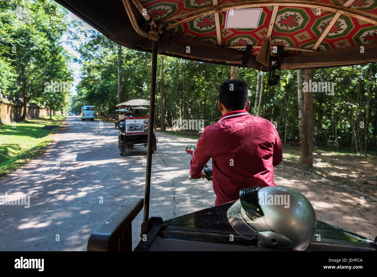 A man drives a rickshaw down a street with a helmet in the back; Cambodia Stock Photo