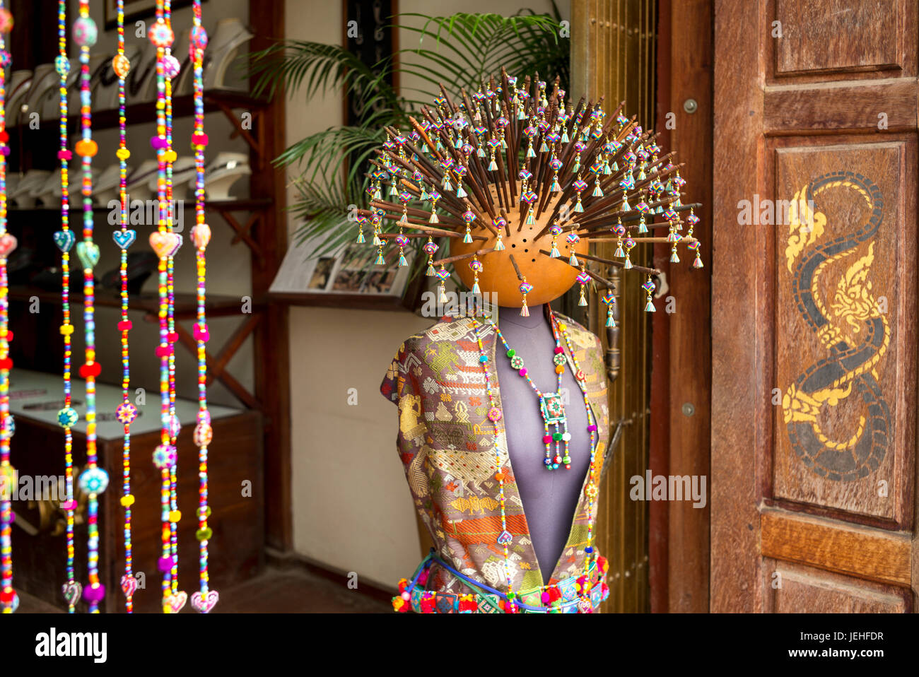 A mannequin wearing traditional Asian clothing, beaded jewelry and numerous sticks with beads sticking out from the head on display Stock Photo