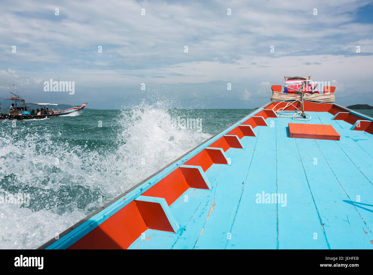 The colourful deck of a painted wooden boat splashing in the Gulf of Thailand with a boat carrying passengers traveling beside it Stock Photo
