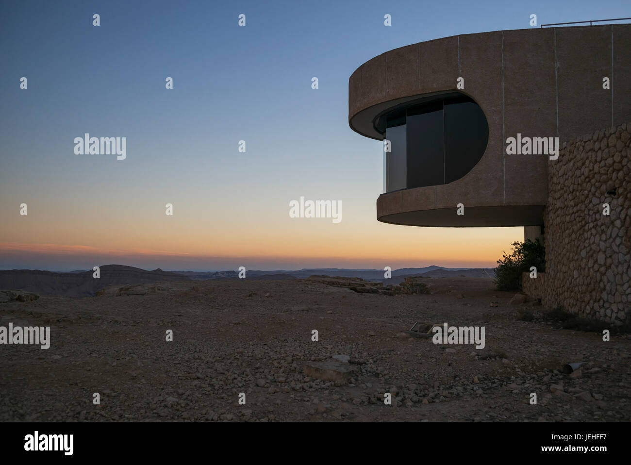 A colourful sunset over the horizon with a viewing window along a curved building for a view; Mitzpe Ramon, South District, Israel Stock Photo