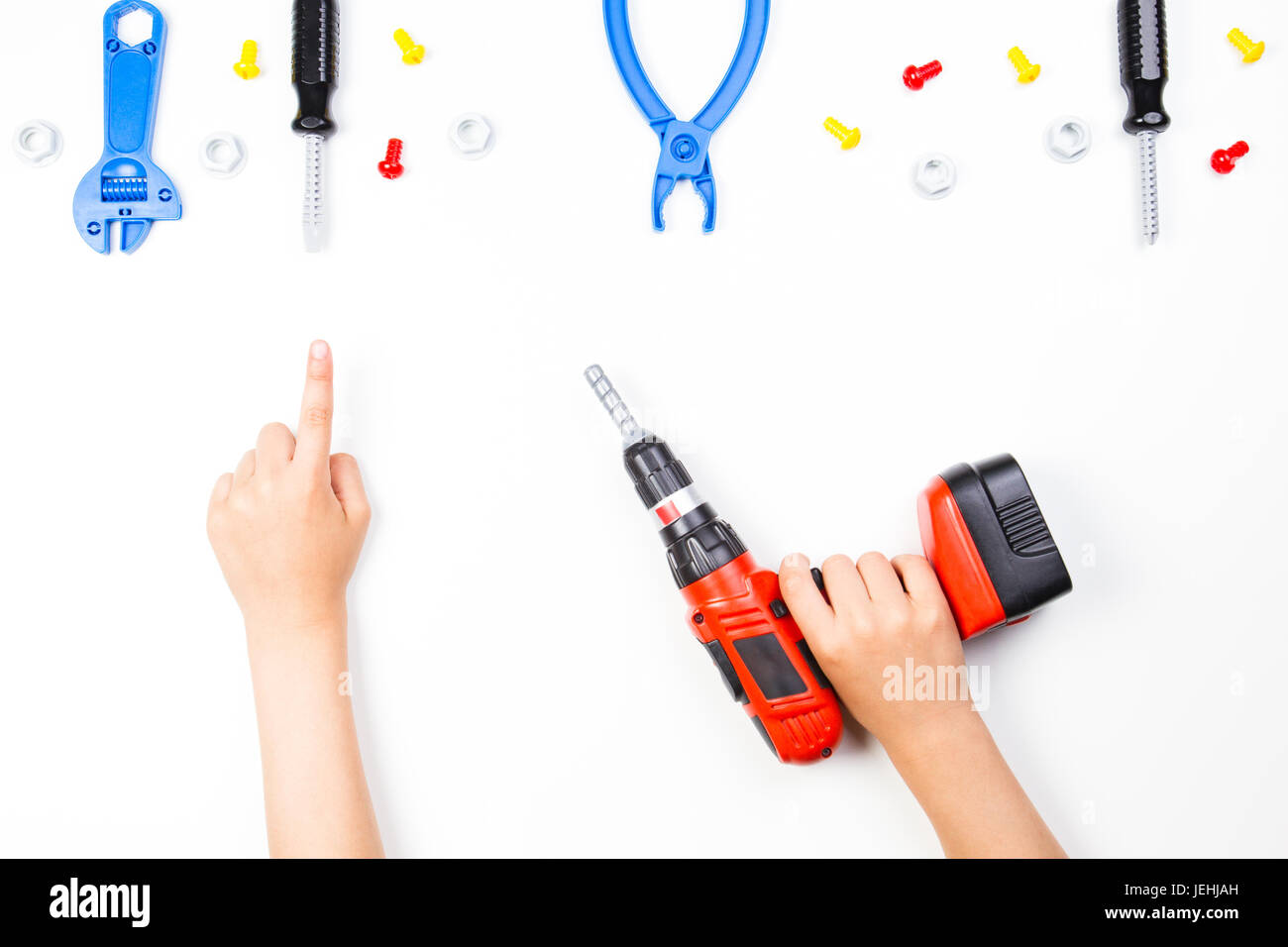 Child's hand holding drill and pointing finger to toys tools on the white background. Stock Photo