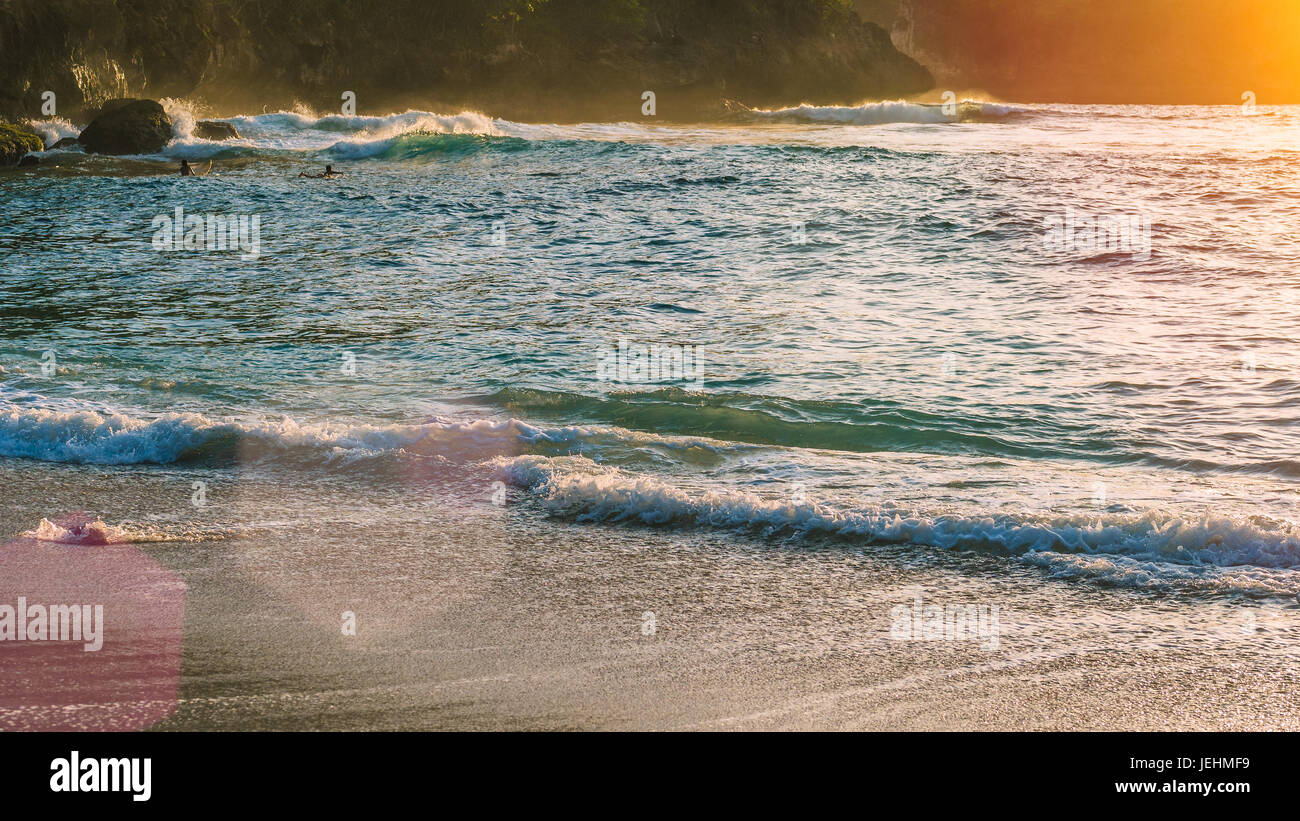 Local kids surf on waves in Sunset light, Beautiful Crystal Bay, Nusa Penida Bali Stock Photo