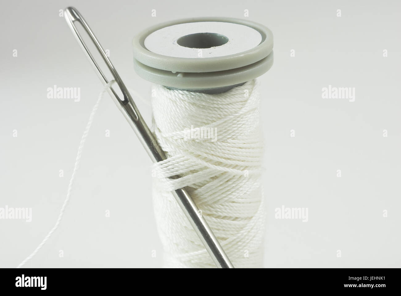 Sewing needle threaded with white cotton, inserted into thread on