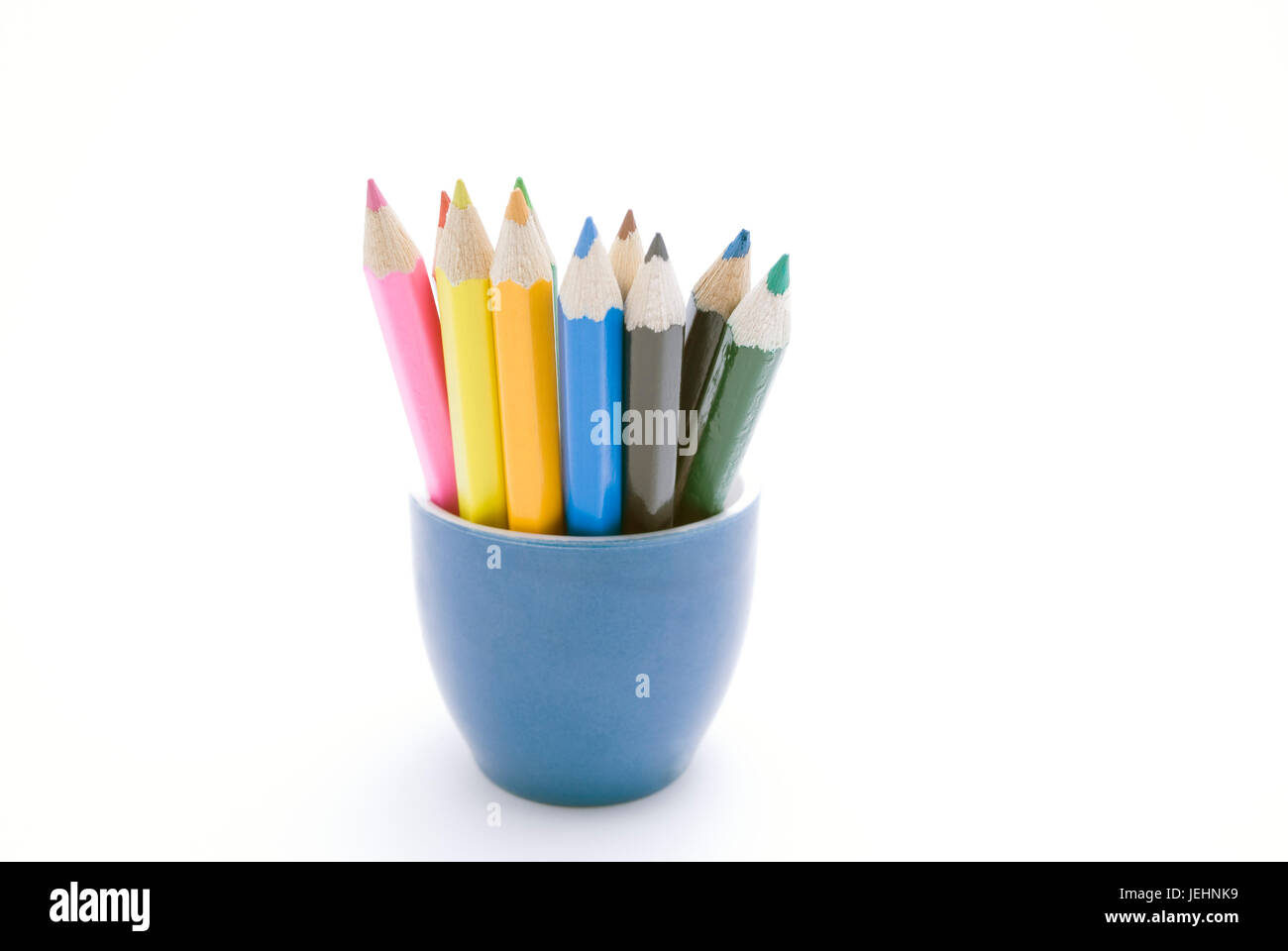 Set of coloured pencils in a blue ceramic container against a white background.  Pencil colours:  pink; red; yellow; green; orange/ochre; light blue;  Stock Photo