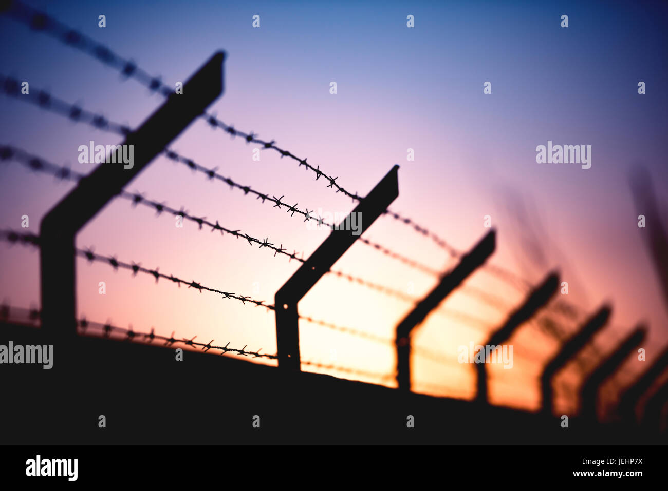 Wall with barbed wire and a sunset in the background. Stock Photo