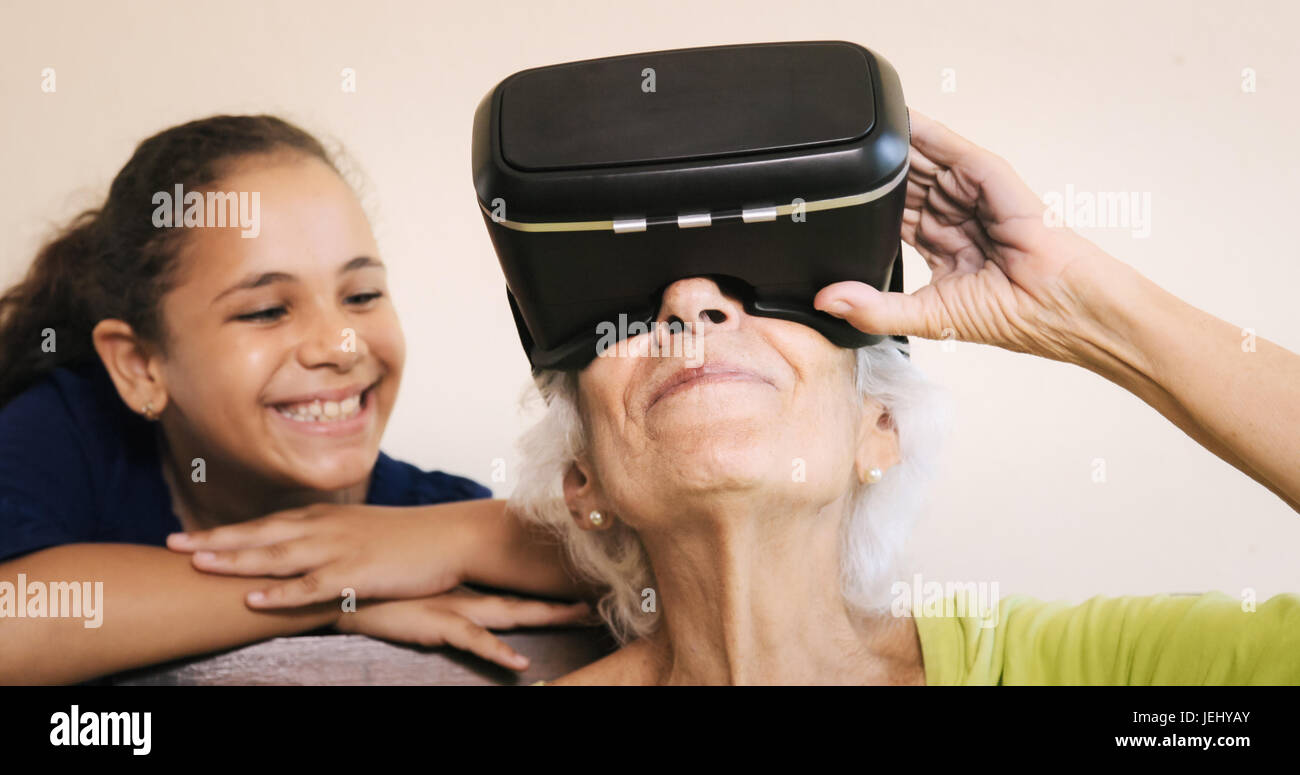 Family relationship between grandmother and granddaughter. Happy old woman playing virtual reality with little girl at home. VR, Augmented Reality vid Stock Photo