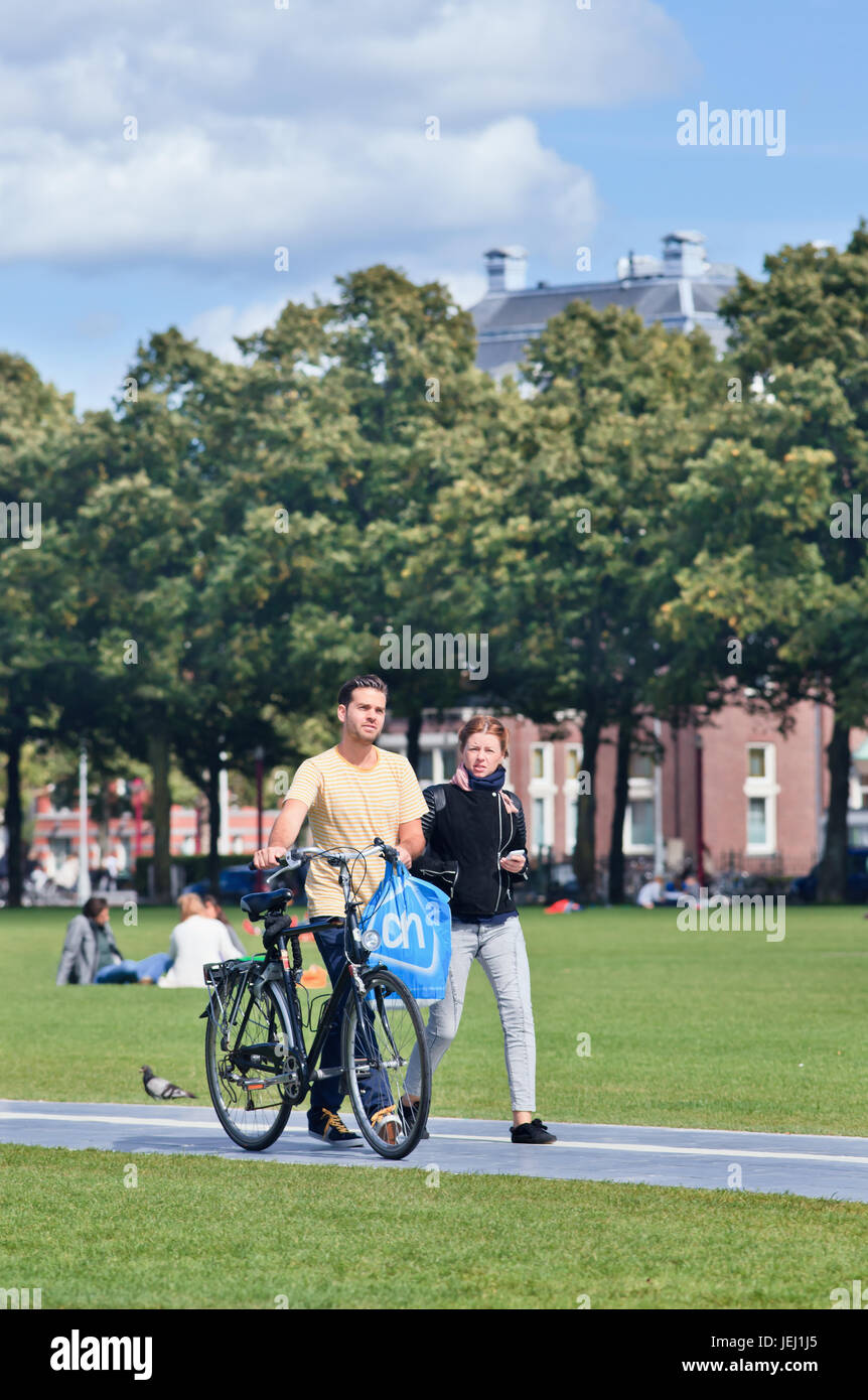 AMSTERDAM-AUG. 24, 2014. Caucasian couple walks on a sunlit Museum Square. A popular touristy square where several famous museums are located. Stock Photo