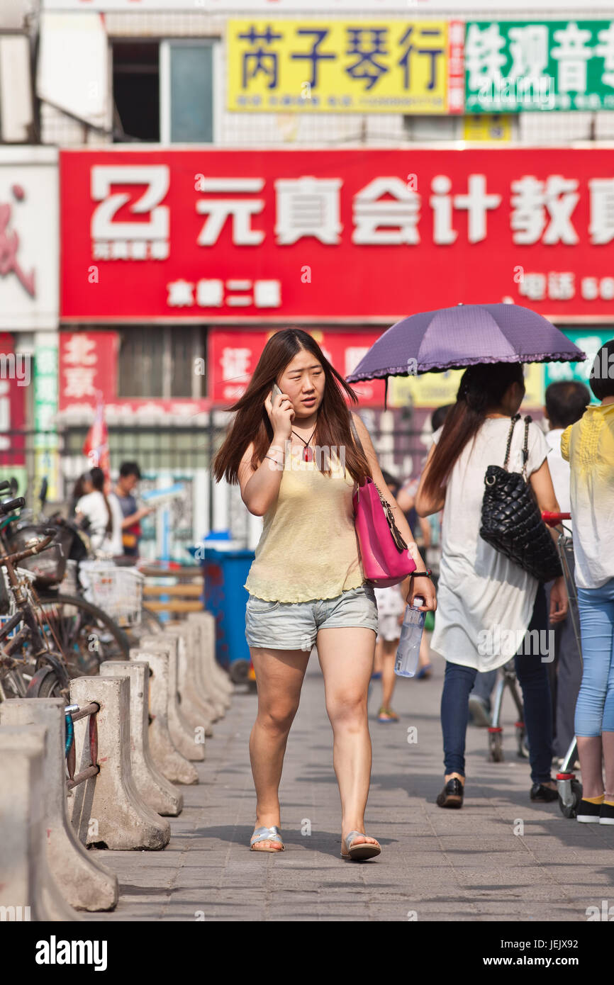 BEIJING-JULY 24, 2015. Girl in a shopping area busy with her smartphone. China has currently 519.7 million smartphone users. Stock Photo