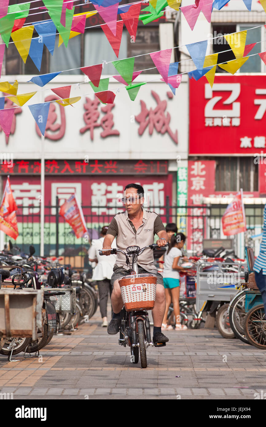 BEIJING-JULY 24, 2015. Man on e-bike in shopping area. In a decade, e-bikes in China climbed from near zero to 150 million (2015). Stock Photo