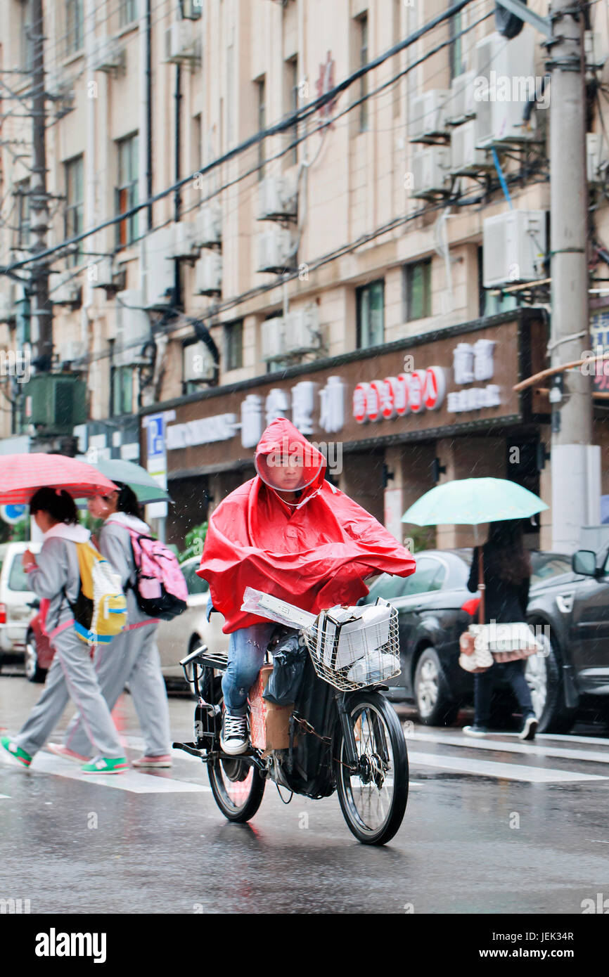 Chinese boy dressed in rainwear on an e-bike. Shanghai has a humid subtropical climate, its summer is very warm and humid. Stock Photo